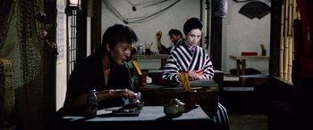 Movie still from “Lady Snowblood” (1973), directed by Toshiya Fujita – A man and a woman sitting at a table with chopsticks in front of them; Medium shot, Over the shoulder angle