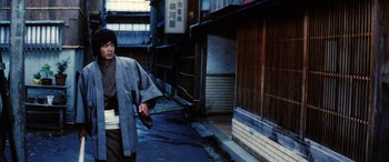 Movie still from “Lady Snowblood” (1973), directed by Toshiya Fujita – A man walking down a street holding a gun; Medium shot, Low angle