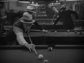Movie still from “Lady for a Day” (1933), directed by Frank Capra – A black and white photo of a man playing a game of billiards; Medium shot, High angle
