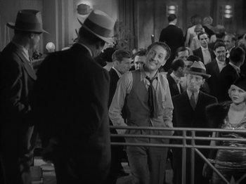 Movie still from “Lady for a Day” (1933), directed by Frank Capra – A man in a suit and tie standing next to a crowd of people; Medium shot, Over the shoulder angle
