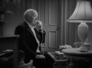 Movie still from “Lady for a Day” (1933), directed by Frank Capra – An older man sitting in a chair talking on a phone; Medium shot, High angle