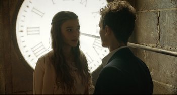 A young man and a young woman standing next to each other in front of a clock tower