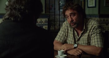 Movie still from “Everybody Knows” (2018), directed by Asghar Farhadi – A man sitting at a table with a cup in front of him; Medium shot, Over the shoulder angle