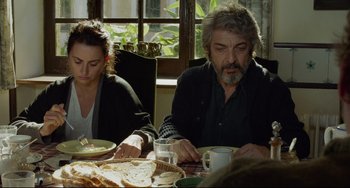 Movie still from “Everybody Knows” (2018), directed by Asghar Farhadi – A man and a woman sitting at a table with plates of food on it; Medium shot, Over the shoulder angle