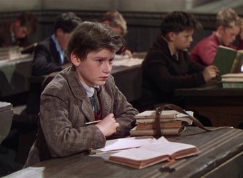 Movie still from “Lassie Come Home” (1943), directed by Fred M. Wilcox – A boy sitting at a table in front of a book; Medium shot, High angle