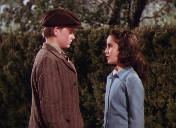 Movie still from “Lassie Come Home” (1943), directed by Fred M. Wilcox – A man and a woman standing next to each other in front of a hedge; Medium shot, High angle