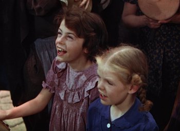 Movie still from “Lassie Come Home” (1943), directed by Fred M. Wilcox – Two young girls are laughing together in front of a group of people; Close Up shot, Low angle
