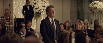 Movie still from “Last Chance Harvey” (2008), directed by Joel Hopkins – A man in a suit and tie standing in front of a group of people; Medium shot, Over the shoulder angle