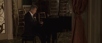 Movie still from “Last Chance Harvey” (2008), directed by Joel Hopkins – A man in a suit playing a piano in a room; Medium shot, High angle
