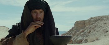 Movie still from “Last Days in the Desert” (2015), directed by Rodrigo García – A man with a black head covering is holding a black bowl; Close Up shot, Low angle