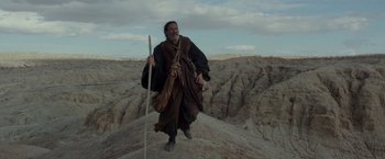 Movie still from “Last Days in the Desert” (2015), directed by Rodrigo García – A man with a long beard and a long stick in the desert; Wide shot, Low angle