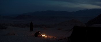 Movie still from “Last Days in the Desert” (2015), directed by Rodrigo García – A person sitting in the sand near a fire; Extreme Wide shot, High angle
