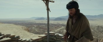 Movie still from “Last Days in the Desert” (2015), directed by Rodrigo García – A man standing on top of a hill next to a tree; Medium shot, Low angle