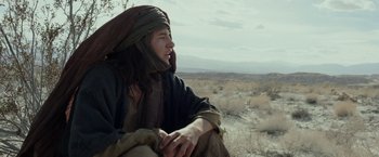 Movie still from “Last Days in the Desert” (2015), directed by Rodrigo García – A man sitting on the side of a road in the middle of the desert; Medium shot, Low angle