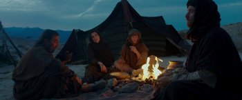 Movie still from “Last Days in the Desert” (2015), directed by Rodrigo García – A couple of people sitting next to a campfire; Medium shot, Low angle