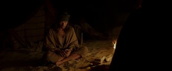 Movie still from “Last Days in the Desert” (2015), directed by Rodrigo García – A man sitting on the ground in front of a fire; Medium shot, High angle