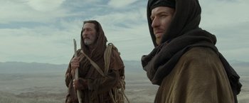 Movie still from “Last Days in the Desert” (2015), directed by Rodrigo García – Two men are standing in the desert while one of them is holding a stick; Medium shot, Low angle