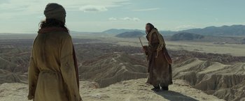 Movie still from “Last Days in the Desert” (2015), directed by Rodrigo García – A man standing on top of a mountain holding a stick; Wide shot, Low angle