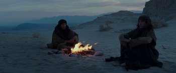 Movie still from “Last Days in the Desert” (2015), directed by Rodrigo García – A man sitting on the ground next to a fire; Wide shot, Over the shoulder angle