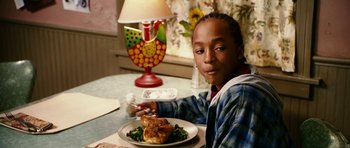 Movie still from “Last Holiday” (2006), directed by Wayne Wang – A young boy sitting at a table with a plate of food on it; Close Up shot, Over the shoulder angle