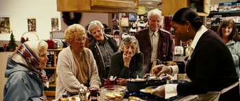 Movie still from “Last Holiday” (2006), directed by Wayne Wang – A group of people sitting at a table with food on it; Medium shot, Over the shoulder angle