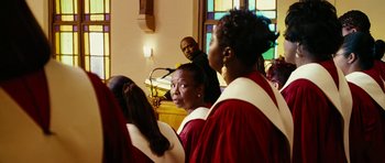 Movie still from “Last Holiday” (2006), directed by Wayne Wang – A group of people standing in front of a stained glass window; Medium shot, Over the shoulder angle