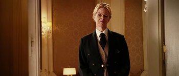 Movie still from “Last Holiday” (2006), directed by Wayne Wang – A man in a suit and tie standing in front of a lamp; Medium shot, Low angle