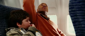 Movie still from “Last Holiday” (2006), directed by Wayne Wang – A man and a boy sitting on a seat on an airplane; Medium shot, Overhead angle