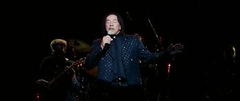 Movie still from “Last Holiday” (2006), directed by Wayne Wang – A man with long black hair is holding a microphone; Medium shot, Low angle