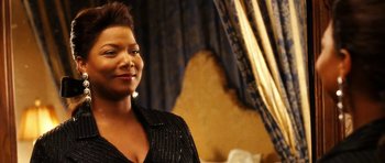 Movie still from “Last Holiday” (2006), directed by Wayne Wang – A woman standing in a room smiling for the camera; Close Up shot, Over the shoulder angle