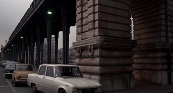 Movie still from “Last Tango in Paris” (1972), directed by Bernardo Bertolucci – A car parked on the side of the road near a building; Wide shot, Low angle