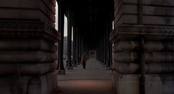Movie still from “Last Tango in Paris” (1972), directed by Bernardo Bertolucci – A person walking down a sidewalk under a bridge; Extreme Wide shot, High angle