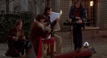 Movie still from “Last Tango in Paris” (1972), directed by Bernardo Bertolucci – A group of people sitting next to each other on a street; Wide shot, High angle