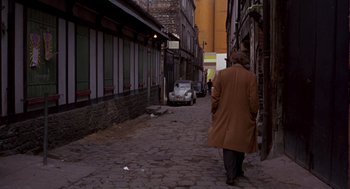 Movie still from “Last Tango in Paris” (1972), directed by Bernardo Bertolucci – A man walking down a street with a car in the background; Extreme Wide shot, High angle