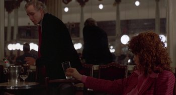 Movie still from “Last Tango in Paris” (1972), directed by Bernardo Bertolucci – A woman sitting at a table holding a glass of wine; Medium shot, Over the shoulder angle