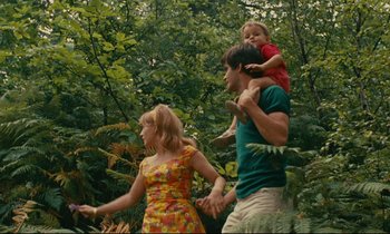 Movie still from “Happiness” (1965), directed by Agnès Varda – A man and a woman holding hands while a child rides on the back of a man's shoulders; Medium shot, High angle