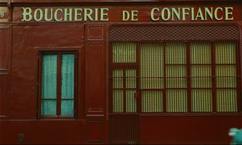 Movie still from “Happiness” (1965), directed by Agnès Varda – A red building with a window and a door on the side of the building; Wide shot, Low angle