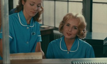 Movie still from “Happiness” (1965), directed by Agnès Varda – Two women in blue uniforms sitting at a table; Medium shot, Over the shoulder angle