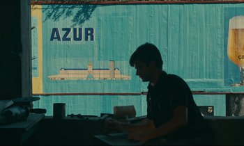 Movie still from “Happiness” (1965), directed by Agnès Varda – A man sitting at a table in front of a building; Extreme Wide shot, Low angle
