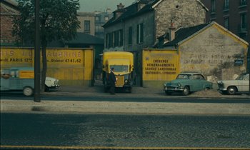 Movie still from “Happiness” (1965), directed by Agnès Varda – A man standing next to a yellow delivery truck on the side of the road; Extreme Wide shot, High angle