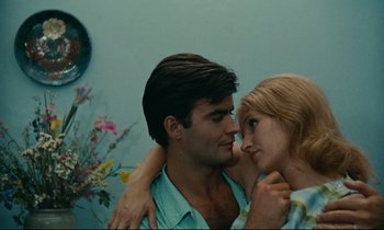 Movie still from “Happiness” (1965), directed by Agnès Varda – A man and a woman embracing each other in front of a blue wall; Close Up shot, High angle