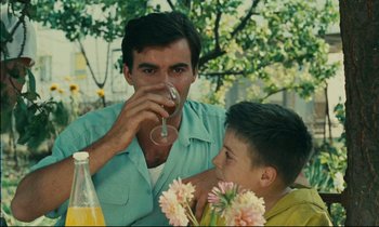 Movie still from “Happiness” (1965), directed by Agnès Varda – A man and a boy sitting at a table drinking wine; Medium shot, Over the shoulder angle