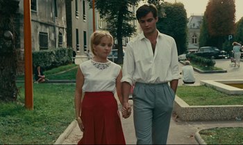 Movie still from “Happiness” (1965), directed by Agnès Varda – A man and a woman holding hands while walking down a sidewalk; Medium shot, Low angle