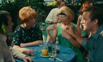 Movie still from “Happiness” (1965), directed by Agnès Varda – A group of people sitting at a table with drinks; Medium shot, Over the shoulder angle
