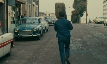 Movie still from “Happiness” (1965), directed by Agnès Varda – A man walking down a street past a row of parked cars; Wide shot, High angle