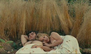 Movie still from “Happiness” (1965), directed by Agnès Varda – A man and a woman laying in a bed next to tall grass; Medium shot, High angle