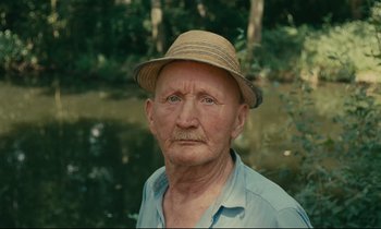 Movie still from “Happiness” (1965), directed by Agnès Varda – An old man wearing a hat near a body of water; Close Up shot, High angle