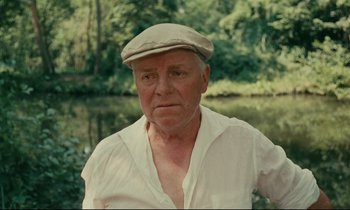 Movie still from “Happiness” (1965), directed by Agnès Varda – An older man wearing a hat near a body of water; Close Up shot, Low angle