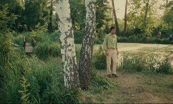 Movie still from “Happiness” (1965), directed by Agnès Varda – A man standing next to two trees in a forest; Wide shot, Over the shoulder angle