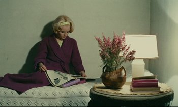 Movie still from “Happiness” (1965), directed by Agnès Varda – A woman sitting on top of a bed next to a table; Medium shot, High angle